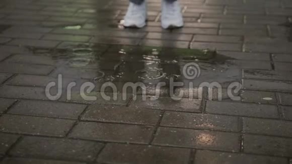 穿着破牛仔裤和白色运动鞋的女人跳进人行道上的水坑里视频的预览图
