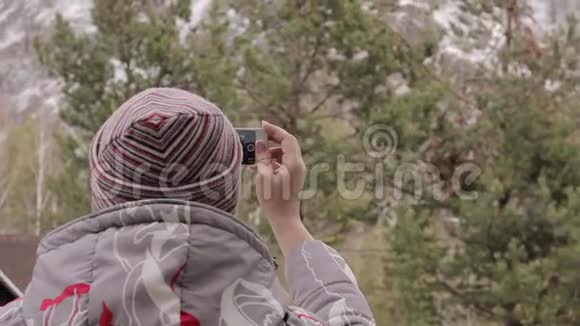 年轻的女游客在她的智能手机上拍照山和松树视频的预览图