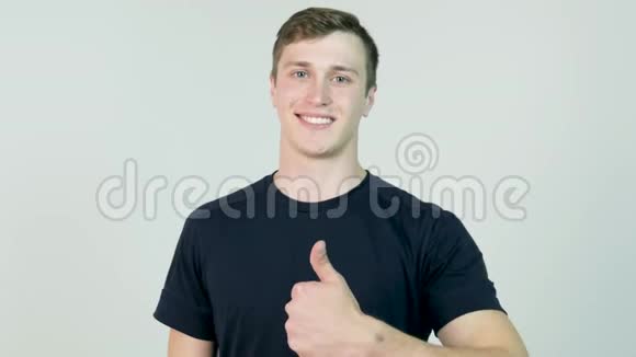 年轻漂亮的男子穿着黑色T恤站在白色背景上看着相机竖起大拇指视频的预览图