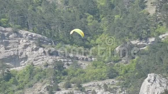 橙色条纹的黄色滑翔伞在灰色大岩石的背景下在美丽的山区飞行视频的预览图
