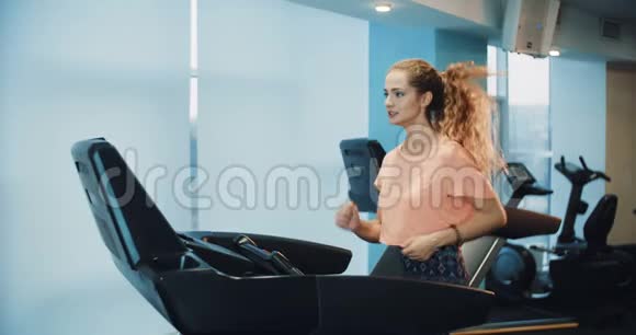 漂亮的卷发女孩在运动健身房的跑步机上跑步视频的预览图