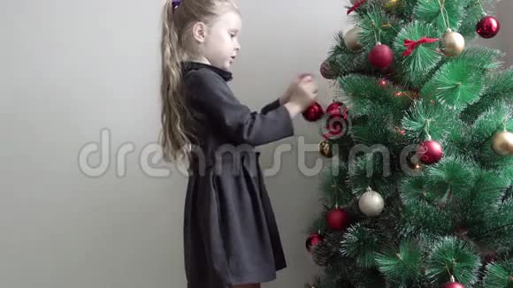 穿着棕色衣服的女孩选择在绿色圣诞树上悬挂一个红色的球以装饰的形式出现视频的预览图