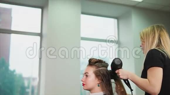 金发的理发师用吹风机和梳子把湿发弄直视频的预览图