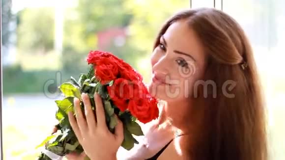 一个年轻的女人在一扇开着的窗户拿着一束红玫瑰一个美丽的女孩喜欢花香视频的预览图