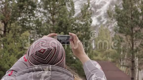 年轻的女游客在她的智能手机上拍照山和松树视频的预览图