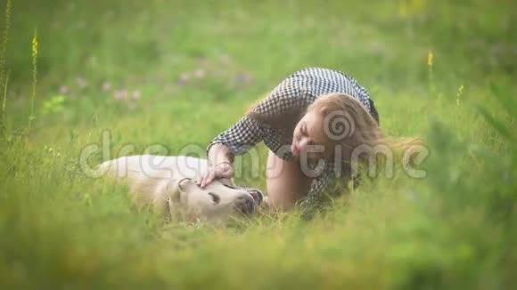 快乐的女主人和她的狗她抚摸着躺在草地上的拉布拉多犬视频的预览图