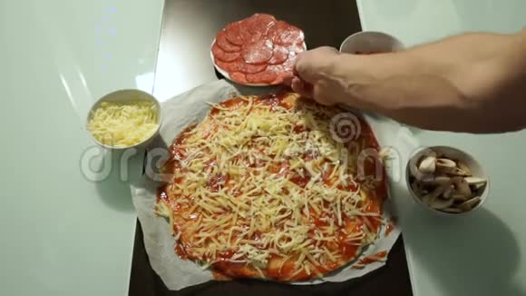 厨师把意大利腊肠放在生披萨的奶酪上视频的预览图