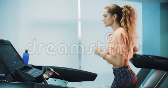 漂亮的卷发女孩在运动健身房的跑步机上跑步视频的预览图