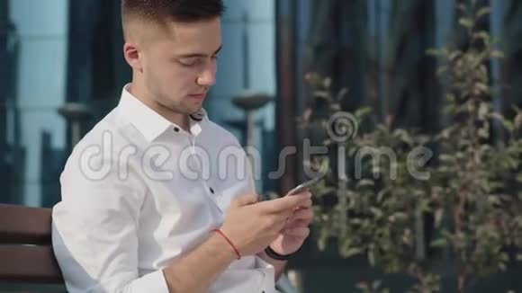 穿白衬衫的男人发短信在城市的智能手机上使用应用程序视频的预览图