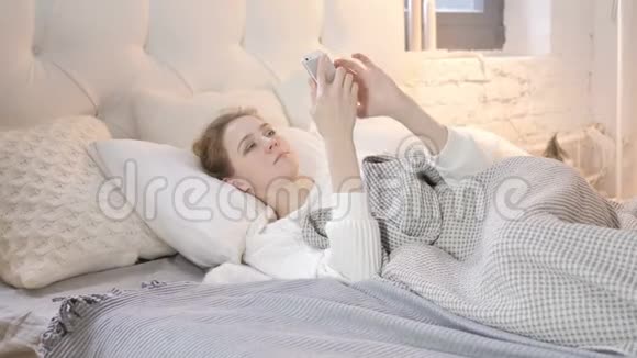 年轻女孩在床上使用智能手机视频的预览图