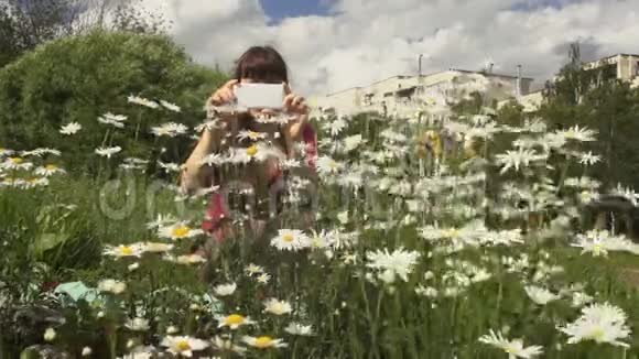 一位年轻女子正在室外用手机拍摄一张洋甘菊的照片视频的预览图