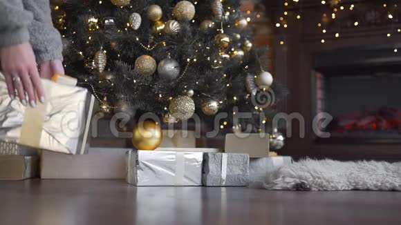 女人手里拿着礼物的盒子放在圣诞树下闪亮的圣诞树花环和球新年视频的预览图