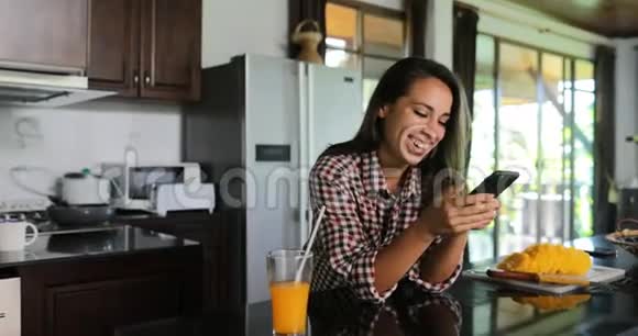 女孩使用手机智能手机在厨房工作室聊天在线年轻女子早晨现代家庭内部视频的预览图