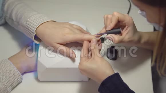 沙龙的指甲护理师傅在一个年轻女人的指甲上涂胶视频的预览图