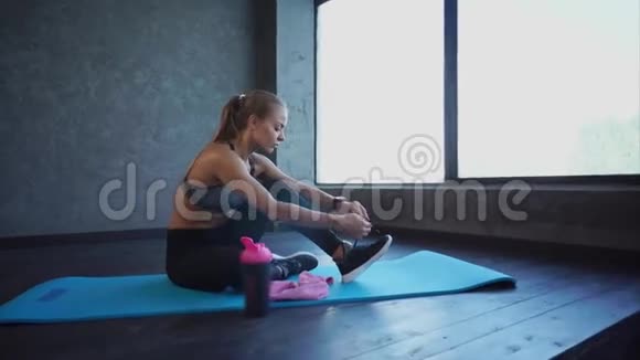 年轻运动员在运动鞋上系鞋带一位女士坐在地毯上做瑜伽视频的预览图