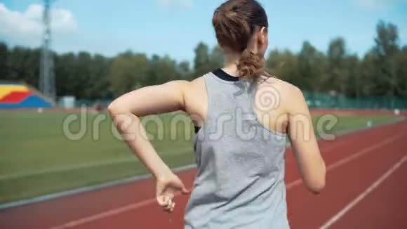 阳光明媚的日子里年轻女子在体育场跑道上跑步视频的预览图