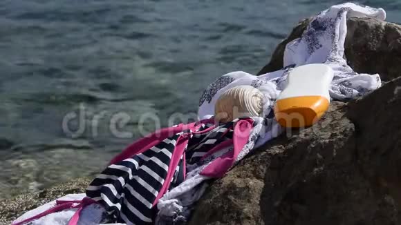 海滩用品泳装防晒霜和海滨岩石上的贝壳视频的预览图
