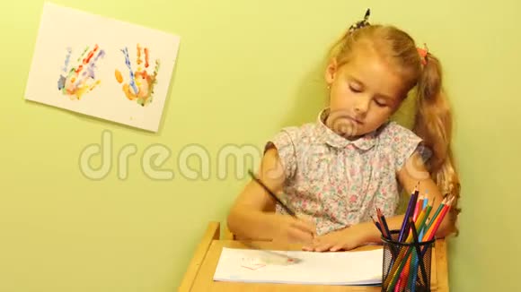 可爱的女孩坐在桌子旁画着家庭肖像有头发尾巴的女孩画画画幸福的家庭视频的预览图