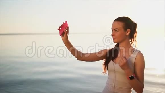 年轻漂亮的女人在海边用智能手机拍自拍照片视频的预览图