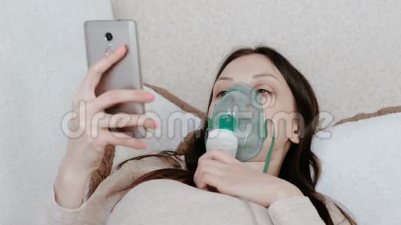使用雾化器和吸入器进行治疗躺在沙发上聊天的年轻女子通过吸入面罩吸入视频的预览图