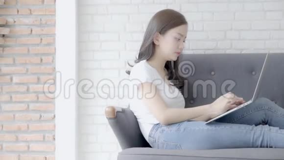 美丽的自由职业年轻的亚洲女性在网上工作手提电脑坐在客厅的沙发上视频的预览图