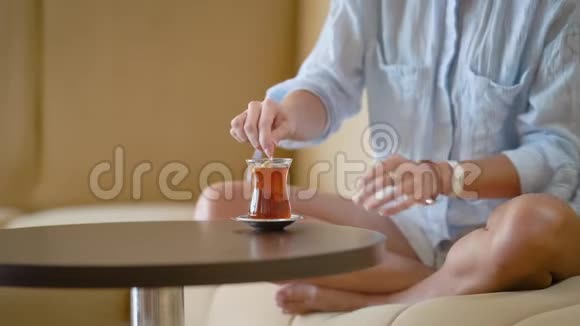 一个女人穿着男人衬衫在杯子里搅拌糖一个女人喝浓茶坐在沙发上双腿抬起视频的预览图