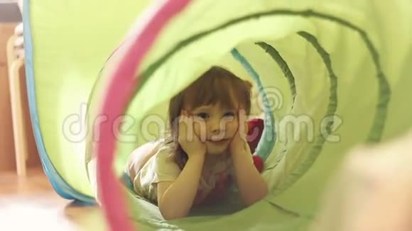 快乐的小女孩在儿童玩具隧道里笑视频的预览图