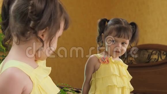 镜子前的小女孩咬着嘴唇镜旁一个穿黄色连衣裙的漂亮孩子有尾巴的女孩视频的预览图
