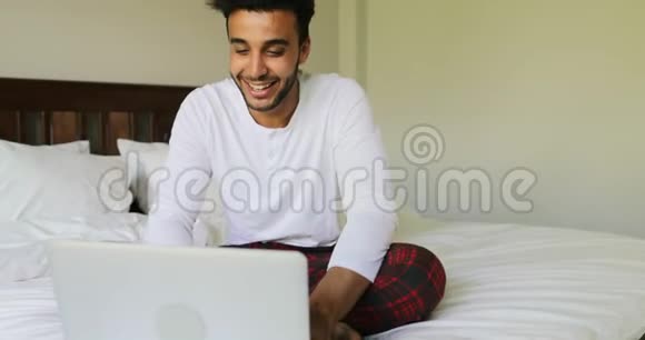 使用笔记本电脑坐在床上的思考者西班牙裔在床上聊天的人视频的预览图