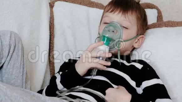 使用雾化器和吸入器进行治疗躺在沙发上的男孩通过吸入器面罩吸入视频的预览图