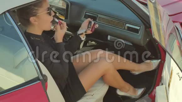 穿高跟鞋的漂亮女人在复古车上涂口红视频的预览图