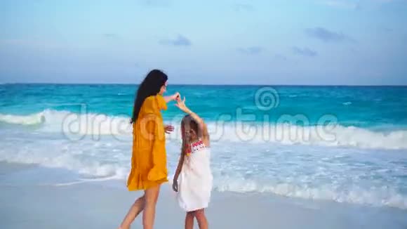 小可爱的女孩和年轻的母亲在温暖的夜晚和美丽的日落热带海滩视频的预览图