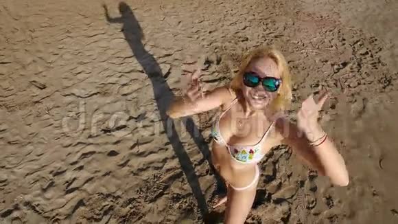 美丽的金发碧眼戴着太阳镜在海滩上拍照视频的预览图