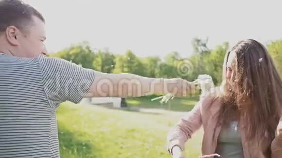 一对浪漫的夫妇在夏天在阳光下的草地上吹着一束蒲公英一起快乐视频的预览图