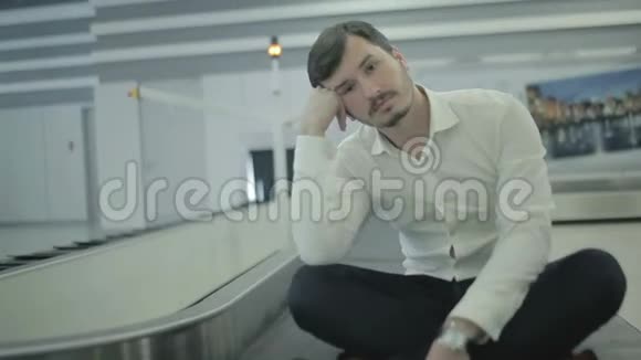无聊的年轻人坐在机场的行李传送带上视频的预览图