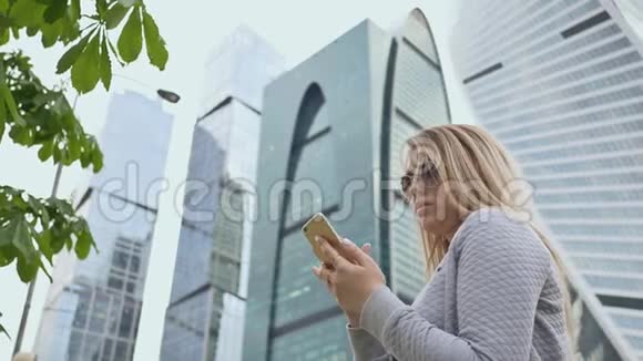 美丽的金发女郎戴着太阳镜在市中心的背景下使用手机视频的预览图