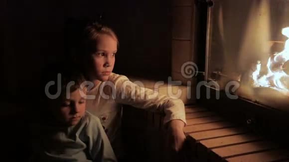 两个悲伤的小孩子坐在壁炉旁看着火视频的预览图