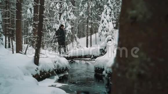 冬日里一个旅行者站在河边在森林里的雪覆盖小径上视频的预览图