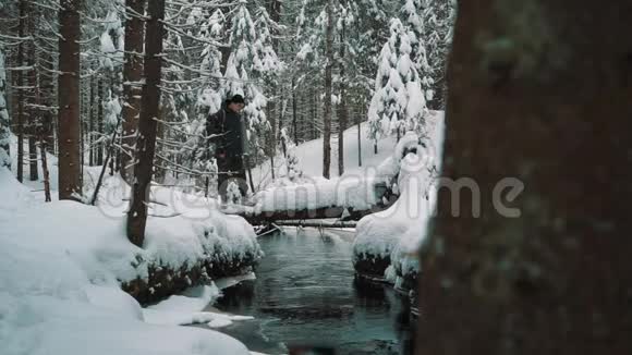 冬天的一天年轻的徒步旅行者站在河边的雪覆盖的小径上视频的预览图