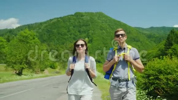 一对年轻的旅游夫妇沿着这条路走到森林覆盖的美丽山脉积极的生活方式和假期视频的预览图