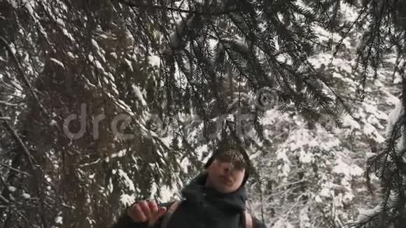 年轻的徒步旅行者在冬日的树林中的雪覆盖小径上触摸树枝视频的预览图