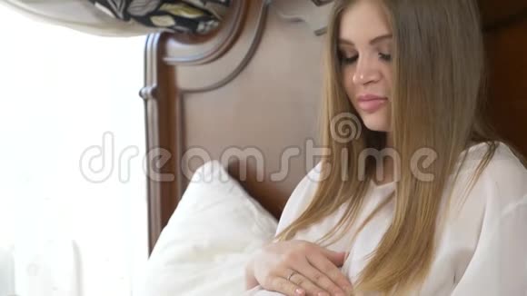 美丽的年轻孕妇抚摸着躺在床上的腹部4k慢动作视频的预览图