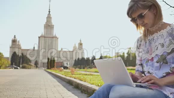 在莫斯科国立大学背景的广场上使用笔记本电脑的女学生视频的预览图