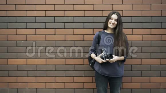 一位年轻女子在砖墙旁边拿着老式相机视频的预览图