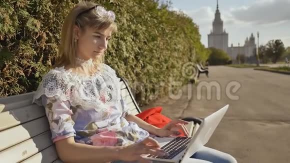 女孩在新鲜空气中打字在键盘上的白色笔记本电脑年轻老练的女人在户外使用笔记本电脑视频的预览图