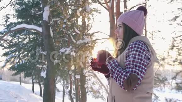 冬天穿着冬衣的女孩在冬天的森林里日落时喝着热覆盖的葡萄酒视频的预览图