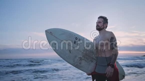 日落时分冲浪者带着冲浪板在海滨散步视频的预览图