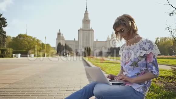 在莫斯科国立大学的背景下在广场上使用笔记本电脑的女学生视频的预览图