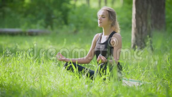 在公园外面做瑜伽的女人她坐在莲花的姿势上视频的预览图