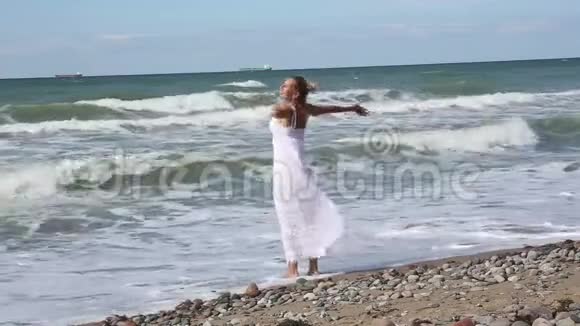 穿着白色裙子的金发女人站在海边张开双臂视频的预览图